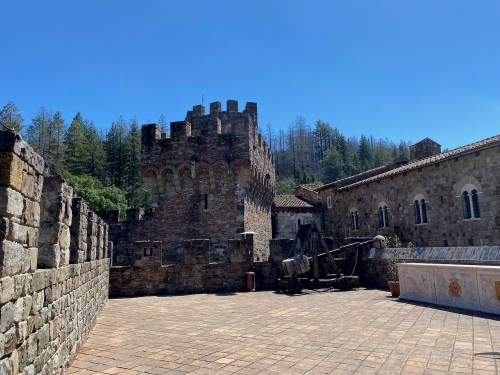 A stone castle with a turret, surrounded by trees, featuring a cannon in the foreground and clear blue skies above.
