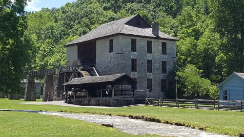 Historic stone mill with a waterwheel, surrounded by lush greenery and a flowing stream.