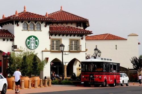 A red trolley bus parked outside a Starbucks with a Spanish-style building and decorative planters.