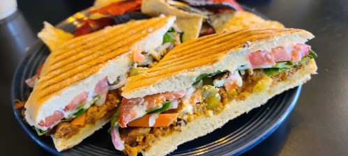 A close-up of a grilled sandwich filled with vegetables, tomatoes, and sauce, served on a plate with chips.