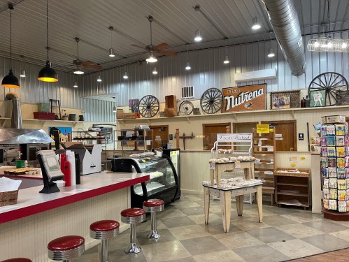 Interior of a rustic store with a counter, stools, shelves, and vintage decor, featuring a sign for "Nutrena."