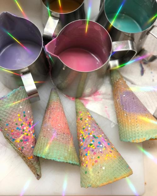 Colorful ice cream cones with sprinkles next to paint-filled cups, creating a vibrant, artistic scene.