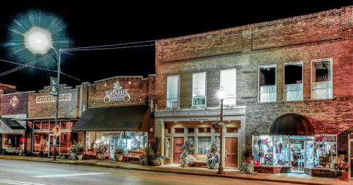 A charming street scene at night featuring brick buildings, shops, and streetlights.