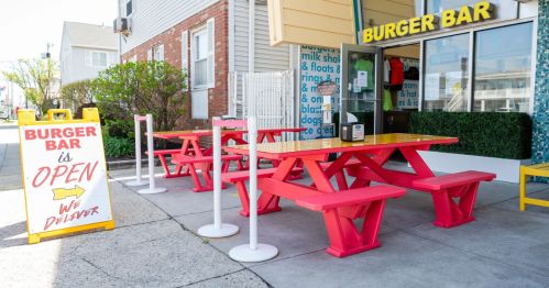 Brightly colored outdoor seating at Burger Bar with a sign indicating it's open and offers delivery.