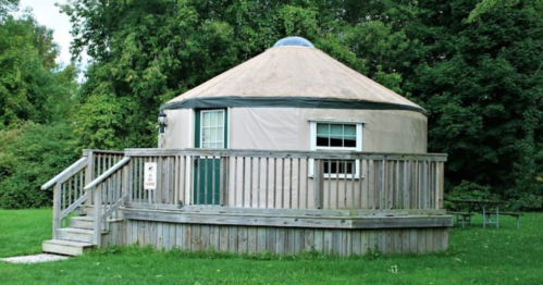 A round yurt with a wooden deck, surrounded by greenery in a park setting.