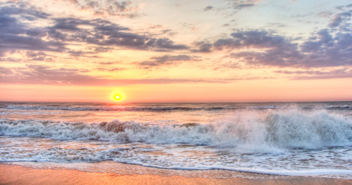 A serene beach scene at sunset, with waves gently crashing and a colorful sky filled with clouds.