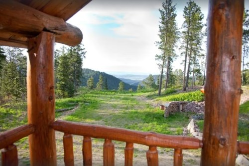 View from a wooden porch overlooking a lush green landscape and distant mountains under a clear sky.
