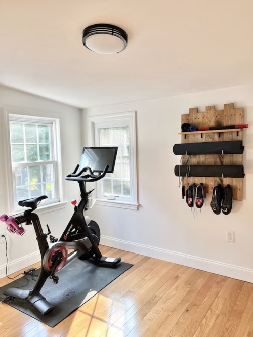 A home gym featuring a stationary bike and a wall rack for shoes and accessories, with natural light from windows.