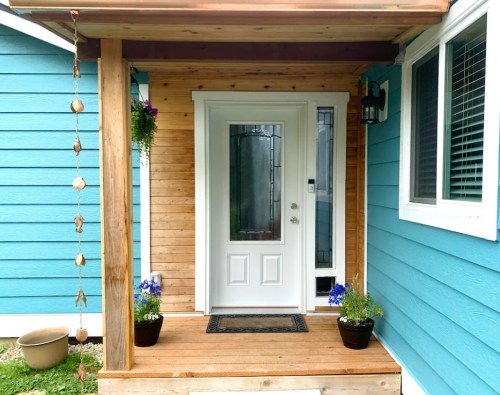 A welcoming entrance with a white door, blue walls, and potted flowers on a wooden porch.