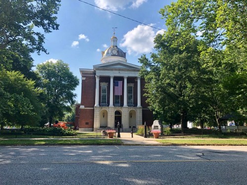 Historic building with a clock tower, American flag, surrounded by trees and a clear blue sky.