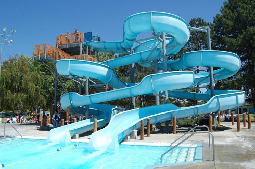 A large, blue water slide structure at a pool, with multiple twisting slides and a clear blue sky in the background.