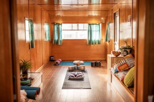 Cozy interior of a wooden room with colorful cushions, plants, and large windows letting in natural light.