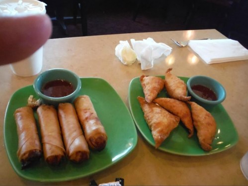 Two plates of appetizers: one with spring rolls and the other with fried pastries, both served with dipping sauces.