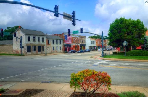 A quaint street scene with historic buildings, traffic lights, and a clock, under a partly cloudy sky.