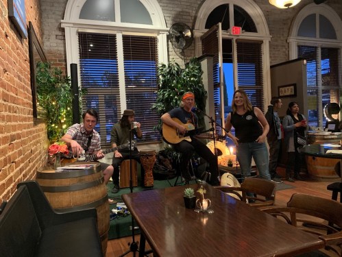 A lively music performance in a cozy venue with musicians playing instruments and a singer engaging the audience.