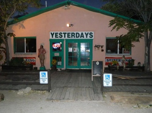 A pink building with green trim, labeled "Yesterdays," featuring an open sign and outdoor seating.