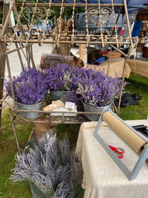 A display of lavender flowers in buckets at a market, with a table and crafting supplies nearby.