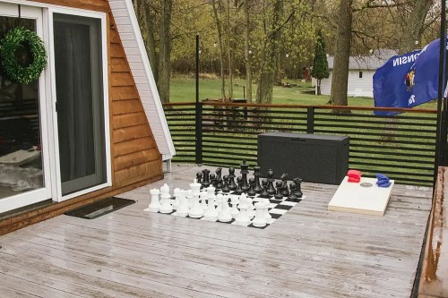 A wooden deck featuring a large outdoor chess set with black and white pieces, a storage box, and a blue flag.
