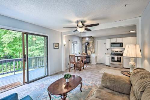 Cozy living space with a sofa, dining area, and kitchen, featuring large windows and a view of greenery outside.