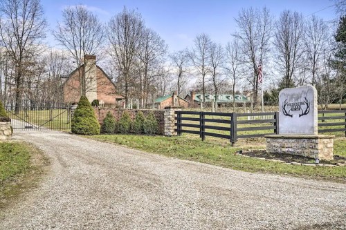 A gravel driveway leads to a brick house, with trees and a decorative stone sign at the entrance.