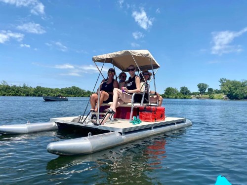 Four people relax on a pontoon boat under a sunny sky, surrounded by water and greenery.