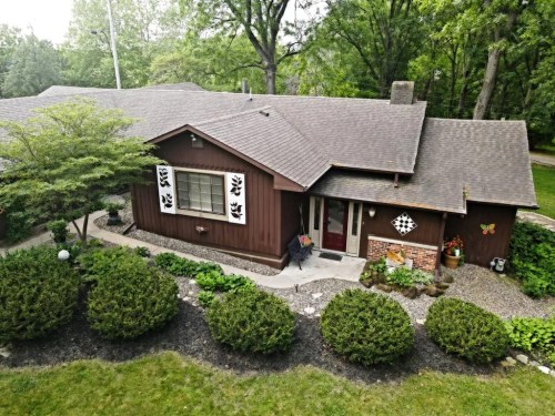 A cozy brown house surrounded by greenery and decorative plants, featuring a stone pathway and butterfly accents.