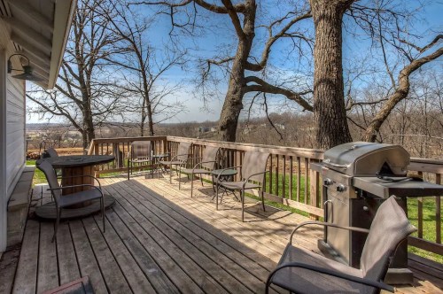 A spacious wooden deck with chairs and a grill, surrounded by trees and a scenic view.