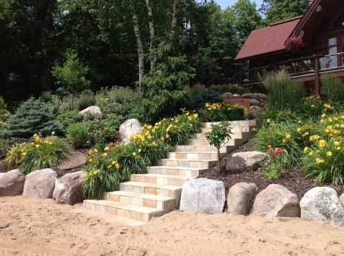 A landscaped garden with stone steps, vibrant flowers, and a wooden house surrounded by trees and rocks.