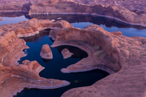 Aerial view of a serene canyon landscape with winding water and rocky formations at dusk.