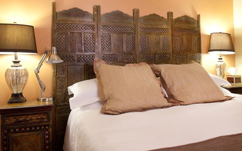 Cozy bedroom with a decorative wooden headboard, two pillows, and stylish lamps on bedside tables.