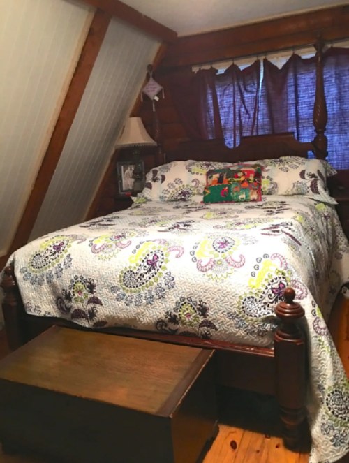Cozy bedroom with a wooden bed, colorful quilt, and a small wooden bench at the foot, set in a rustic cabin.
