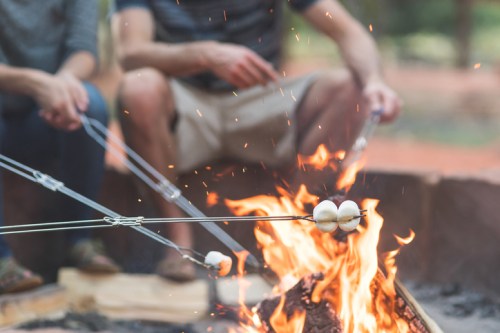 Two people roast marshmallows over a campfire, with sparks flying and a cozy outdoor setting.