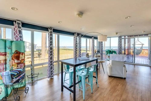 Bright, modern living space with large windows, a dining table, and a view of the outdoors. Coastal decor accents.