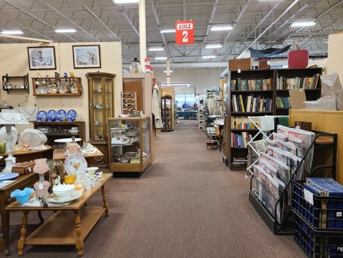 Aisle in an antique store filled with furniture, collectibles, and books, with displays on either side.