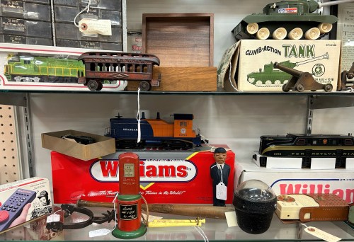 A display of vintage toys and collectibles, including a train, a tank, and various nostalgic items on a glass shelf.
