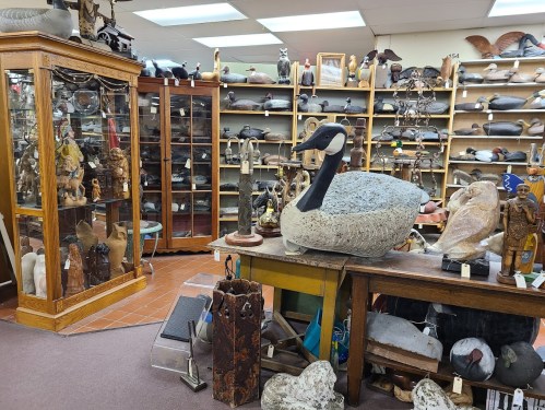 A cozy antique shop filled with various sculptures, carvings, and decorative items, including a large stone goose.