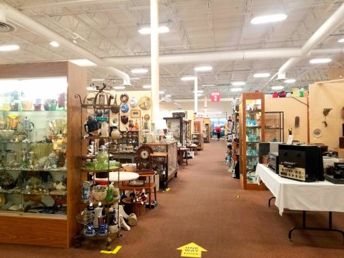 A spacious antique store aisle lined with shelves of vintage items, glassware, and collectibles.