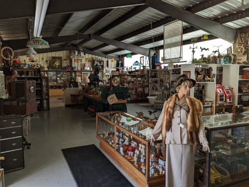 A vintage shop interior filled with antiques, collectibles, and a mannequin dressed in a stylish outfit.