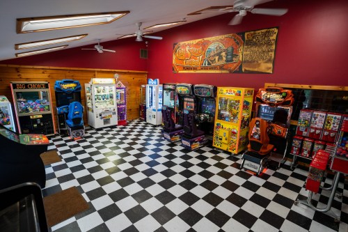 A colorful arcade room with various gaming machines and a checkered floor, featuring bright lights and seating areas.