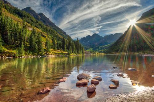 A serene lake surrounded by mountains and lush trees, with sunlight reflecting on the water's surface.