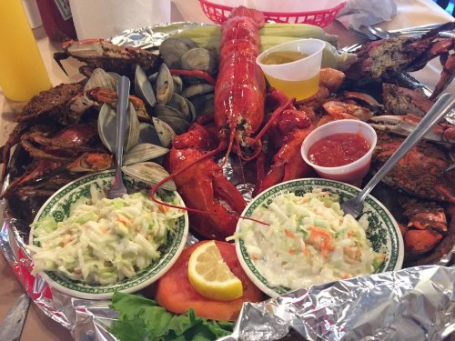 A seafood platter featuring lobster, crabs, clams, and two bowls of coleslaw, garnished with lemon and sauces.
