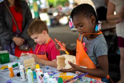Two children are painting wooden crafts at a table, surrounded by colorful paints and art supplies.