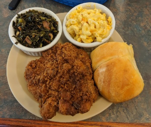 A plate with fried chicken, macaroni and cheese, collard greens, and two dinner rolls.