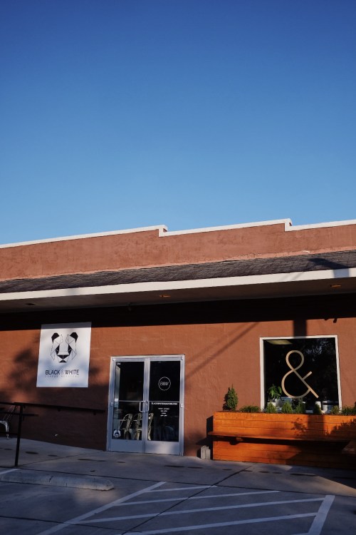 Exterior of a building with a sign reading "Black & White" and a large window displaying a decorative "&" symbol.