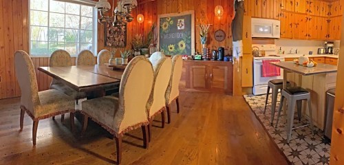 Cozy dining area with a large wooden table, upholstered chairs, and a kitchen featuring modern appliances and wooden accents.