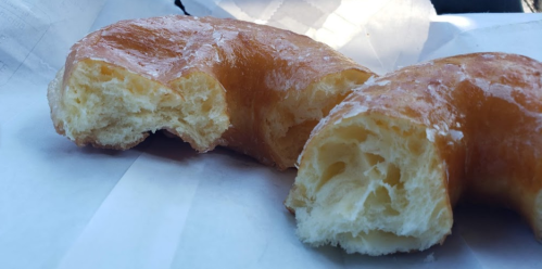 A close-up of a glazed donut, partially bitten, resting on white paper.