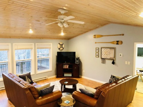 Cozy living room with wooden ceiling, two brown sofas, a coffee table, and a TV, featuring decorative paddles on the wall.