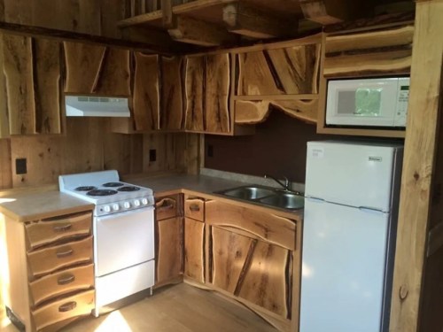 Rustic kitchen with wooden cabinets, a stove, sink, and refrigerator, featuring natural wood textures and a cozy design.