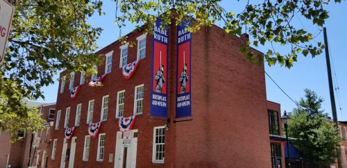 Historic brick building adorned with banners and patriotic decorations, surrounded by trees and a clear blue sky.