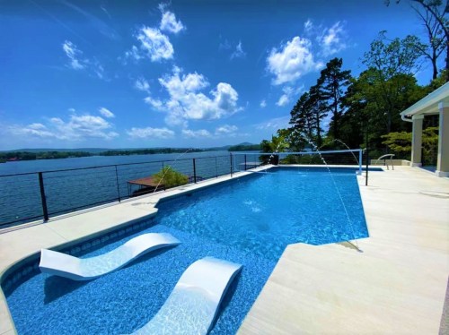 A serene poolside view overlooking a lake, with clear blue water and lush greenery under a bright sky.